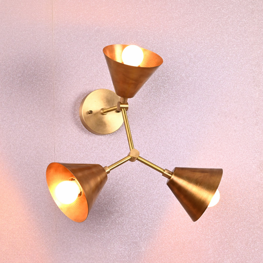 Elegant brass wall sconce with three conical shades arranged in a triangular pattern, designed by Brass Leaf Studio.