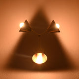 Three-light brass wall sconce glowing warmly, casting a triangular shadow pattern on the wall for ambient lighting.