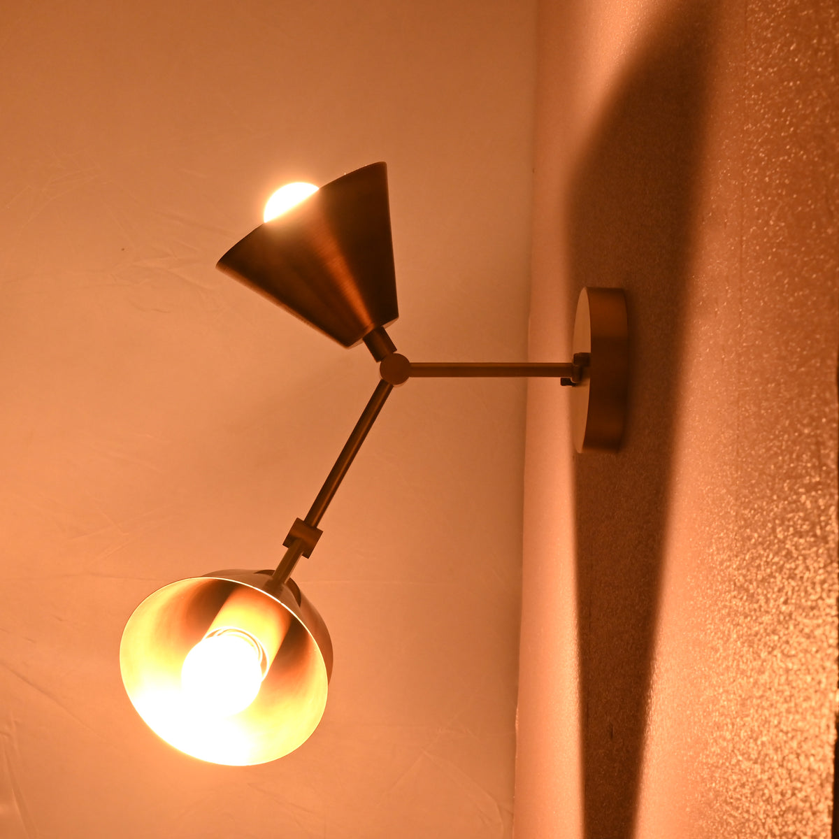 Brass 3-light sconce glowing warmly, photographed from the side to highlight light projection and fixture build.