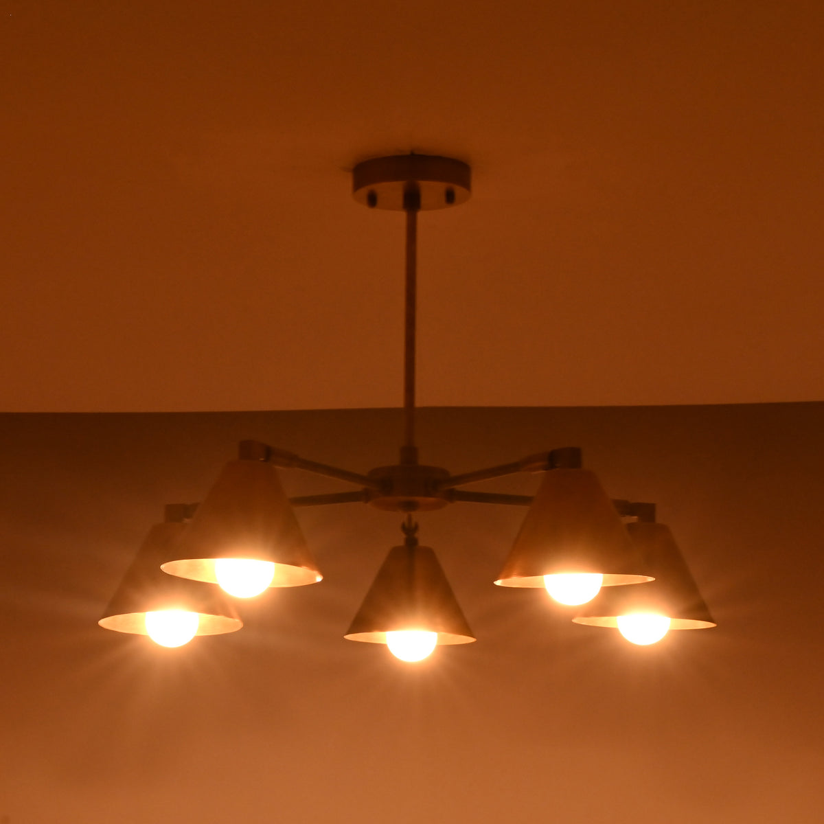 Brass chandelier with five cone shades casting a soft amber glow, ideal for living rooms and bedrooms.
