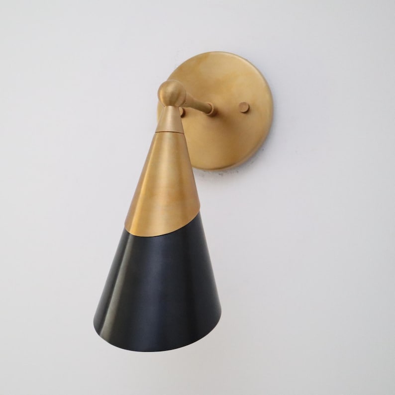 Two-tone brass and matte black cone wall sconce with round brass backplate, angled side view on white wall.
