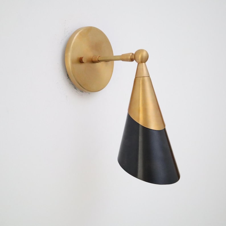 Two-tone brass and matte black cone wall sconce with round brass backplate, angled side view on white wall.