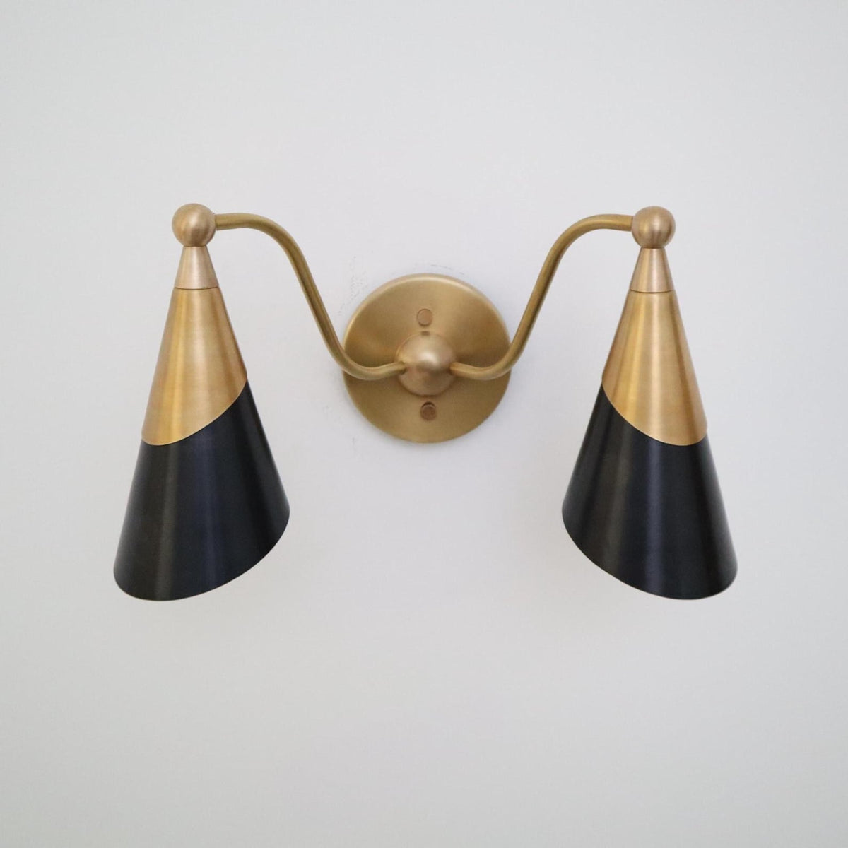 Symmetrical double cone wall sconce in brushed brass and matte black with curved arms and circular brass wall mount.