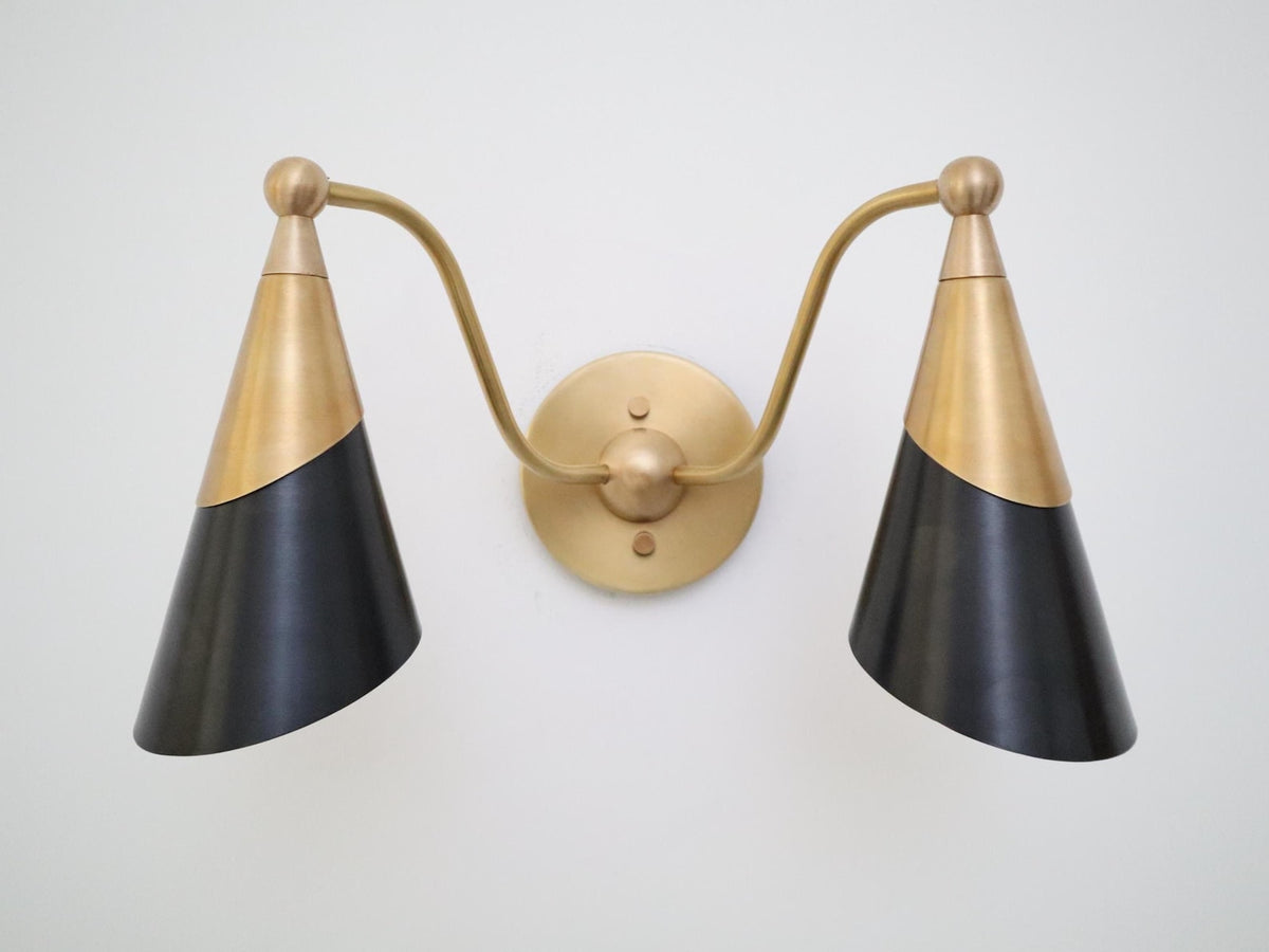 Front view of a brass and matte black twin cone wall light with curved brass arms and round center backplate.