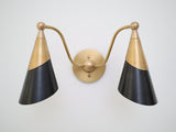 Front view of a brass and matte black twin cone wall light with curved brass arms and round center backplate.
