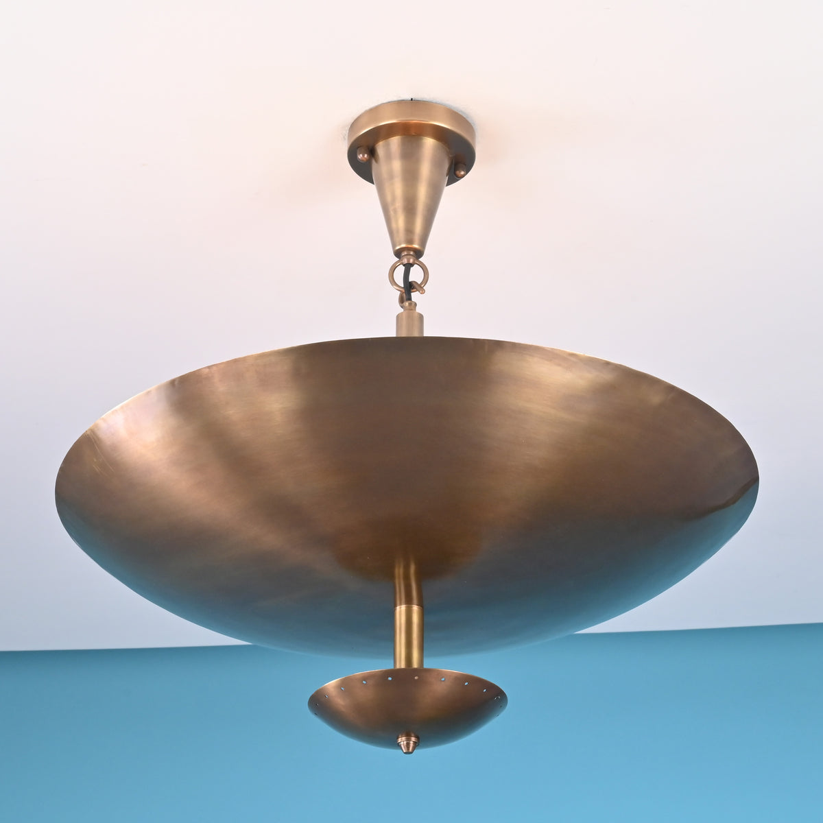 Side view of brushed brass bowl chandelier mounted on a white ceiling against a blue wall.