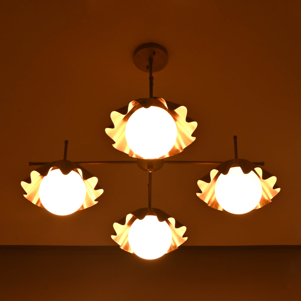 Brass chandelier with four ruffled globe shades glowing warmly in dim light, creating cozy ambient atmosphere for modern interiors.