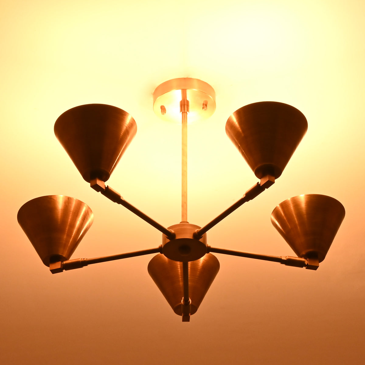 Brass cone chandelier glowing with warm amber light in a dark room, creating an elegant ceiling centerpiece.