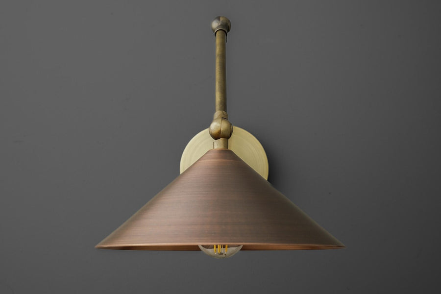 Adjustable brass swing arm wall sconce with cone shade and round backplate, modern industrial wall lamp on gray wall.