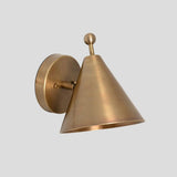 Handcrafted solid brass cone wall sconce with a ball accent on top, mounted on a round brass base, shown at a side angle.