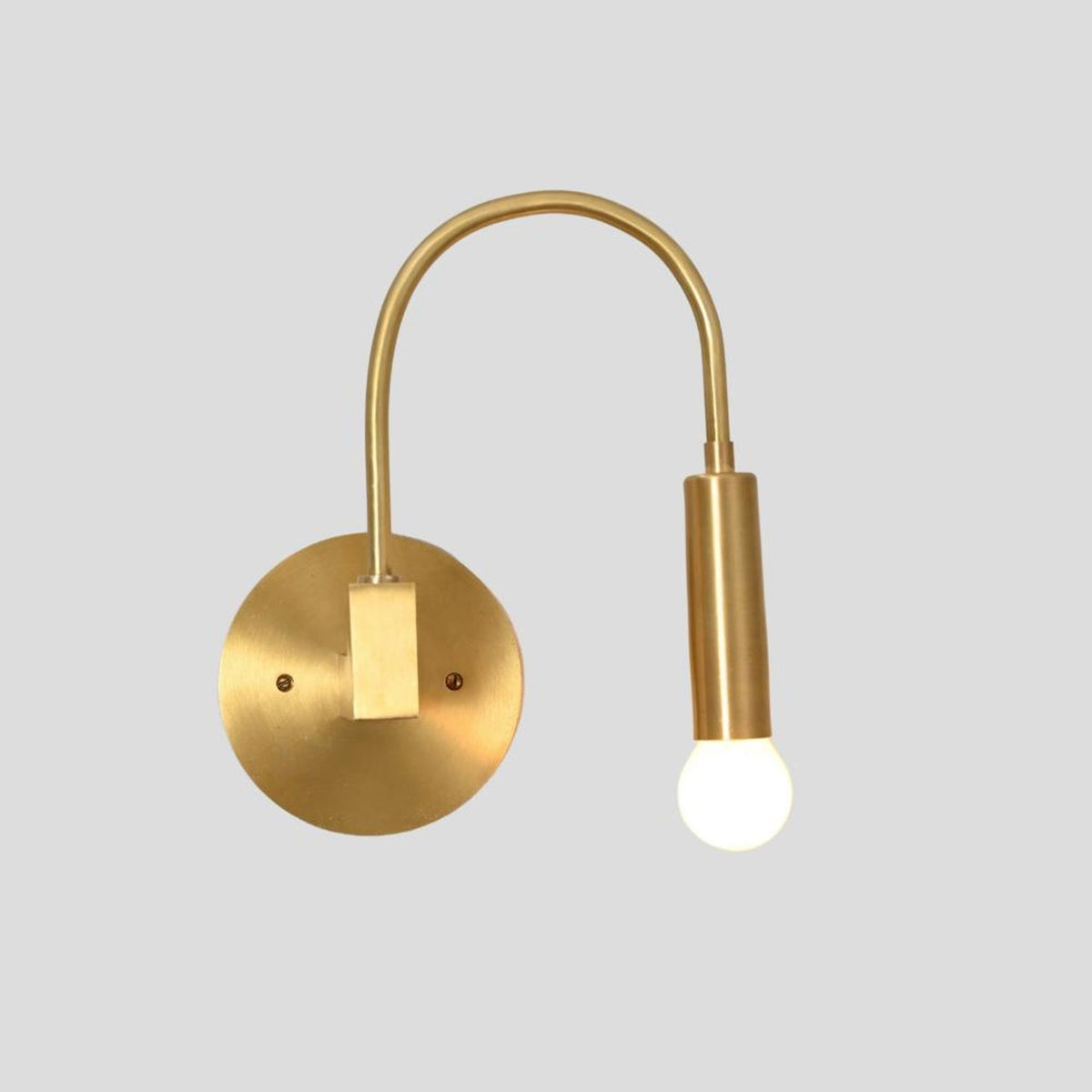 Modern brass wall sconce with curved arm design and exposed bulb, angled front view highlighting circular brass wall mount.