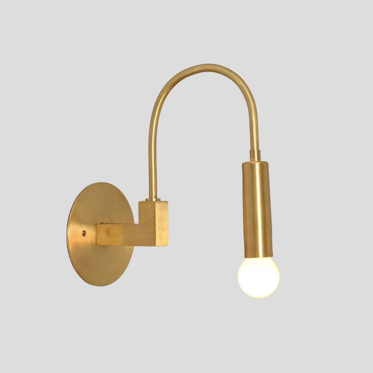 Perspective angle of handcrafted brass wall sconce with arched arm, cylindrical bulb holder, and round wall mount.