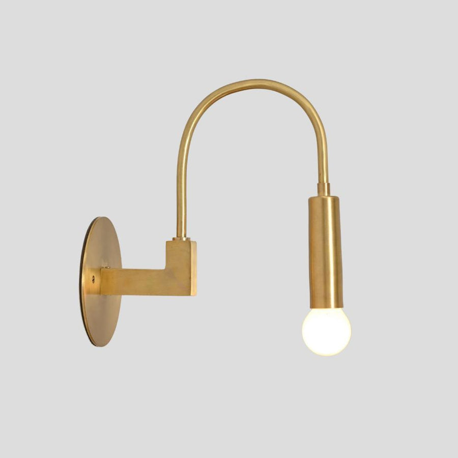 Handmade brass wall sconce with curved arm and exposed bulb, side profile view mounted on round brass base.