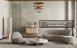 Minimalist sitting area with curvy sofas and a sculptural brass disc chandelier hanging above, adding elegance to a neutral interior