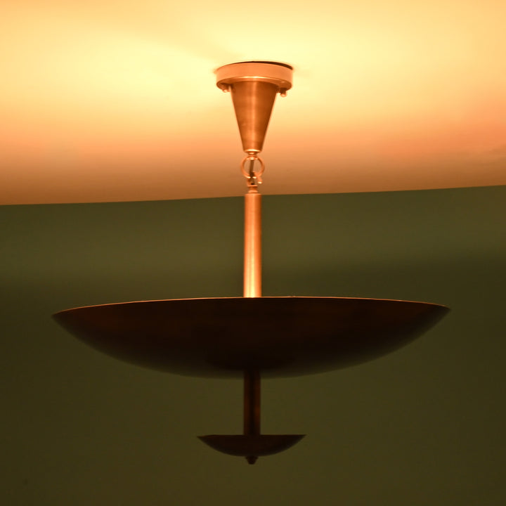 Brass bowl chandelier casting a warm ambient light, viewed from the side against a green background.
