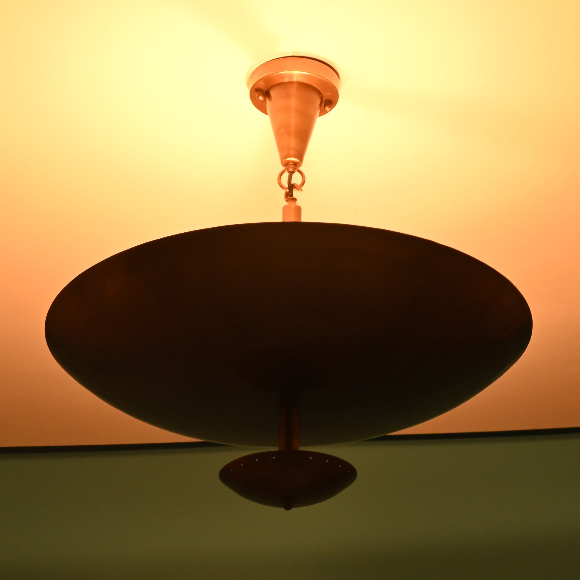 Close-up of a brass bowl chandelier lit warmly, casting an ambient upward glow on the ceiling.