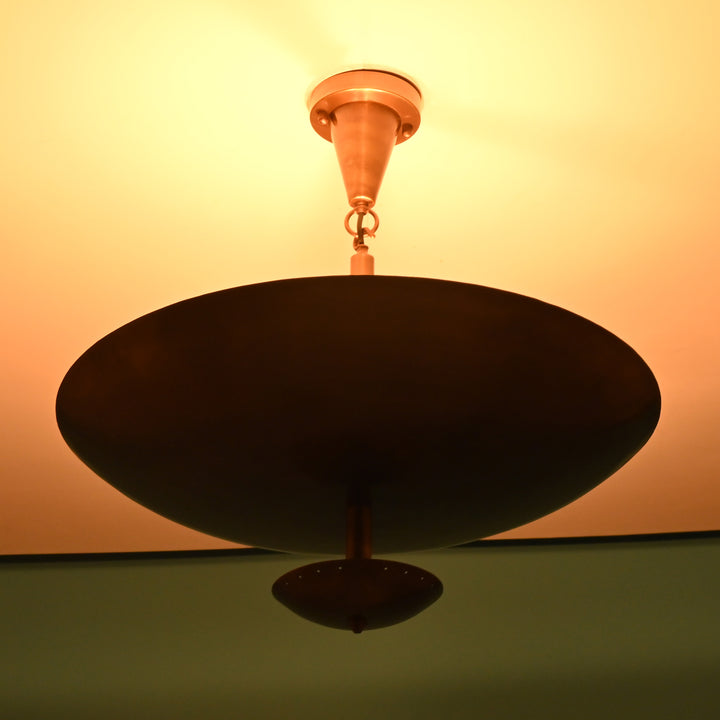 Close-up of a brass bowl chandelier lit warmly, casting an ambient upward glow on the ceiling.