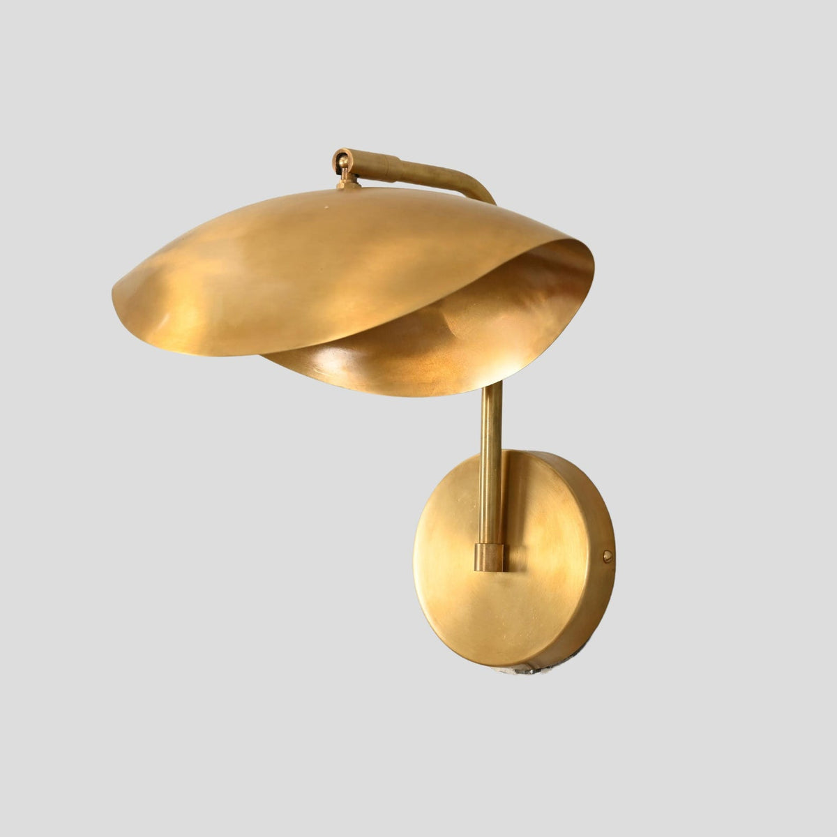 Modern brass wall sconce with sculpted dome shade, angled view showing artistic curvature and round wall mount.