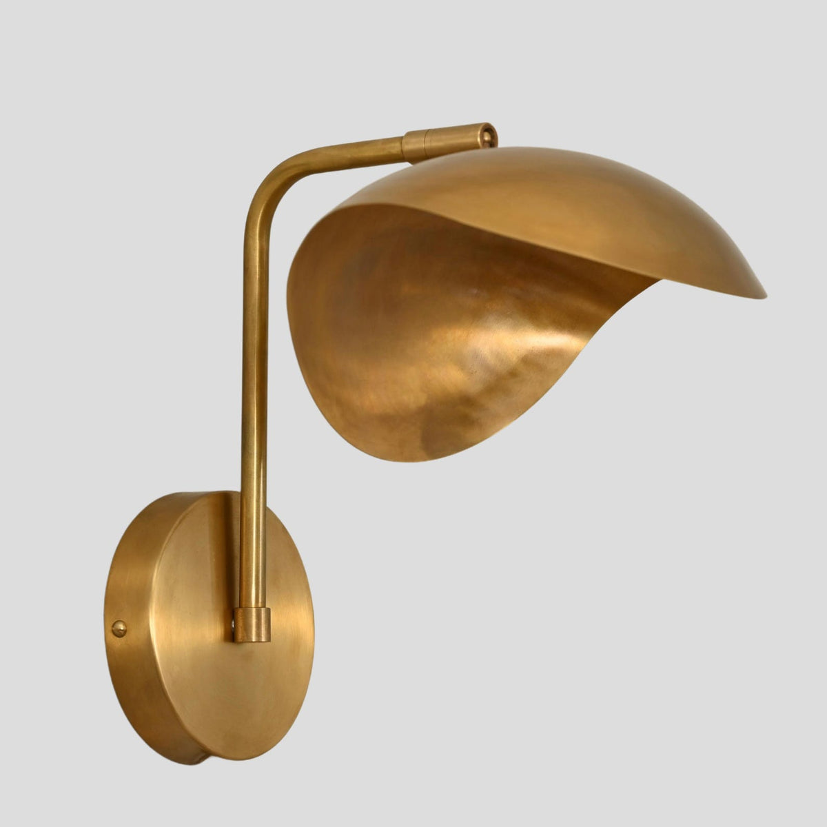 Minimalist brass wall sconce with sculptural dome shade and circular base, perspective view showcasing elegant design.