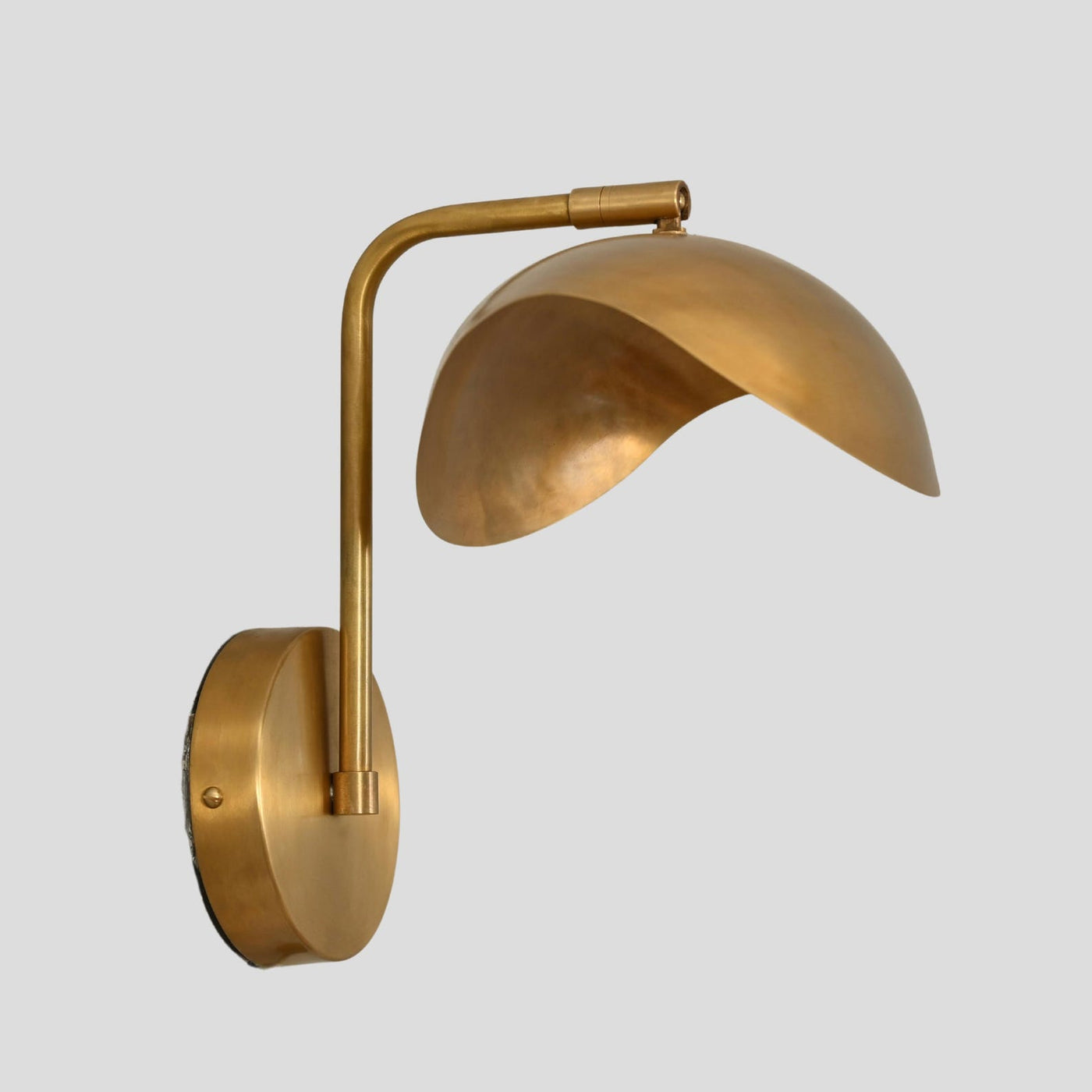 Handmade brass wall sconce with curved dome shade, side profile view, mounted on circular brass base.