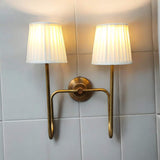 Brass wall sconce with pleated lampshades mounted on tiled wall, providing warm, cozy lighting in bathroom setting.