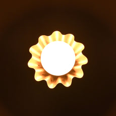 Overhead view of glowing brass flower wall light radiating warm light with wavy petal design.