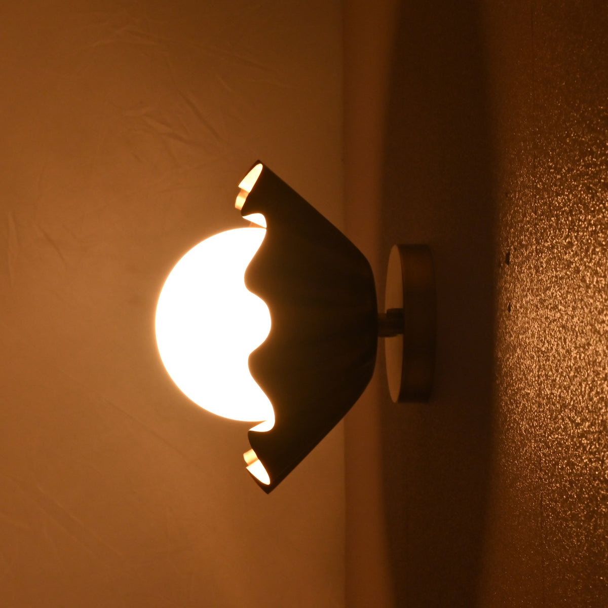Side angle view of brass flower wall light glowing warmly on a wall in a dim environment.