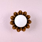 Brass flower wall sconce with round bulb and petal-shaped design viewed from the top against a textured wall.
