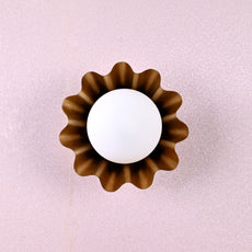 Brass flower wall sconce with round bulb and petal-shaped design viewed from the top against a textured wall.