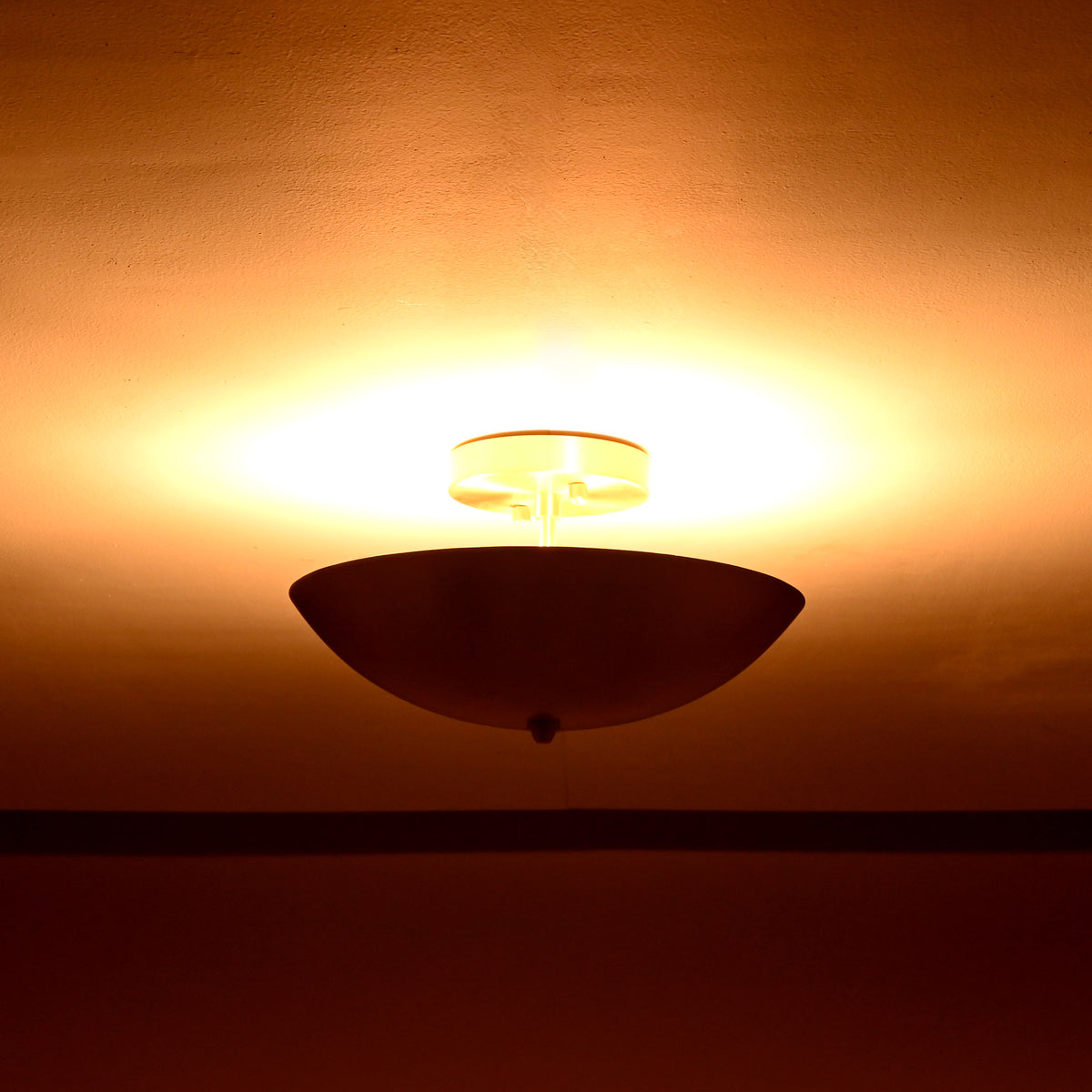 Elegant brushed brass ceiling light glowing warmly in softly lit interior setting