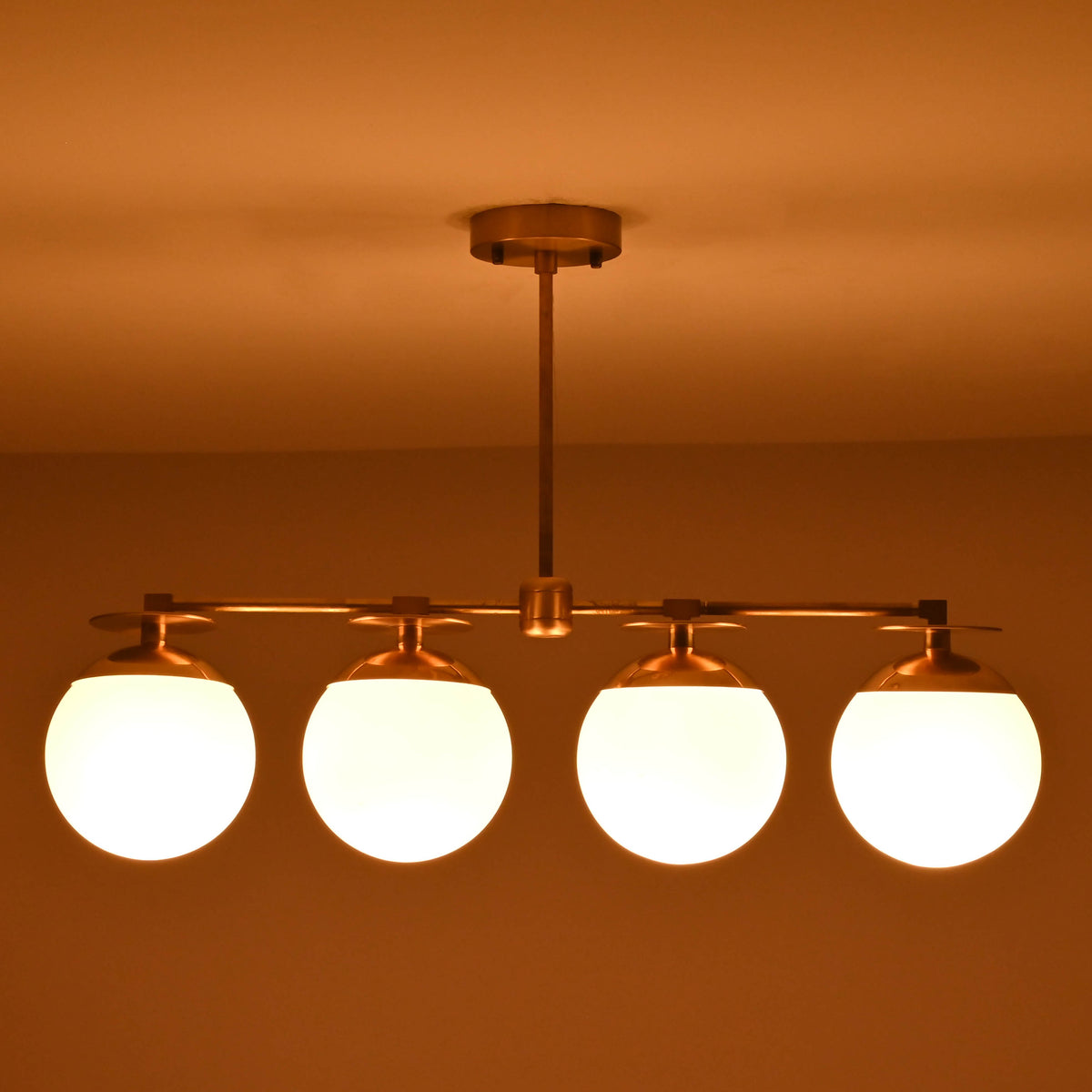 Handmade brass chandelier with four frosted globe shades glowing warmly at night, offering ambient light for dining or living spaces.
