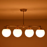 Handmade brass chandelier with four frosted globe shades glowing warmly at night, offering ambient light for dining or living spaces.