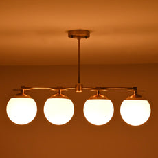 Handmade brass chandelier with four frosted globe shades glowing warmly at night, offering ambient light for dining or living spaces.