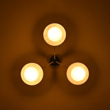 Overhead view of brass chandelier with three frosted globes glowing in the dark, disc shades casting a warm golden halo effect.