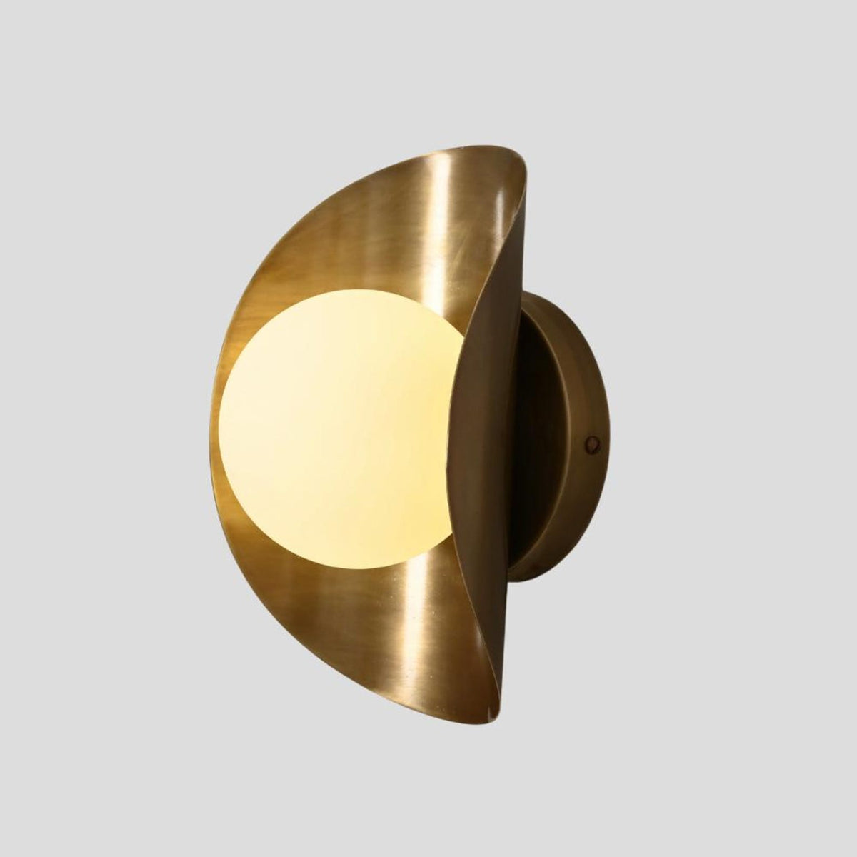 Angled view of brass wall sconce with frosted glass globe illuminated, blending industrial and modern aesthetics.