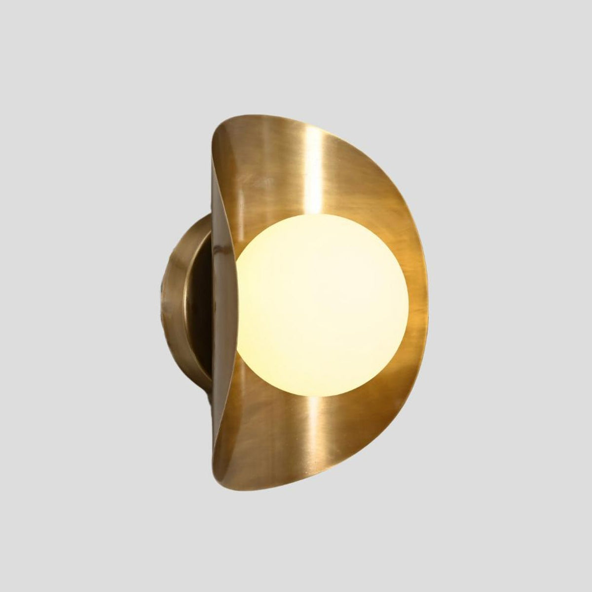 Modern brass wall sconce with frosted glass globe lit up, highlighting warm ambient glow and brushed brass frame.