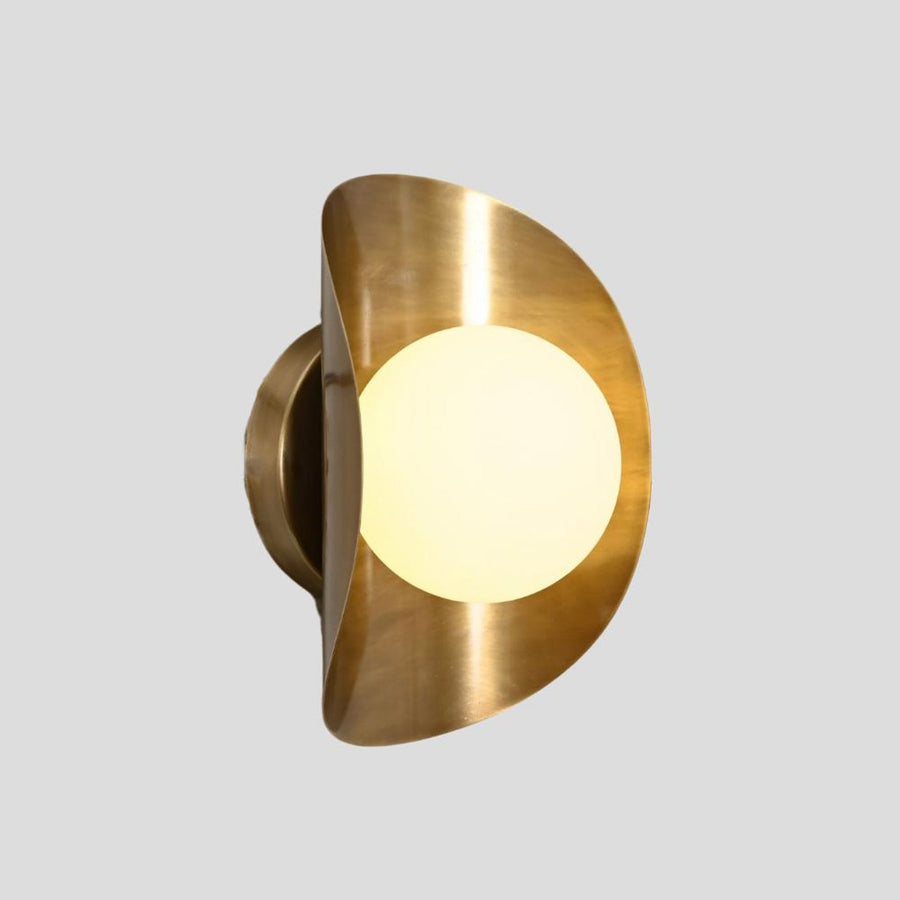 Handmade brass wall sconce with frosted glass globe shade, side profile view showcasing curved brass design.