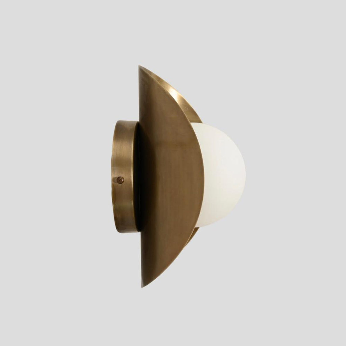 Slim side view of handcrafted brass wall sconce with frosted glass globe shade and brushed brass base.