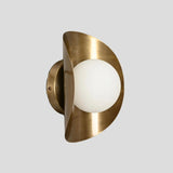 Handmade brass wall sconce with frosted glass globe shade, side profile view showcasing curved brass design.