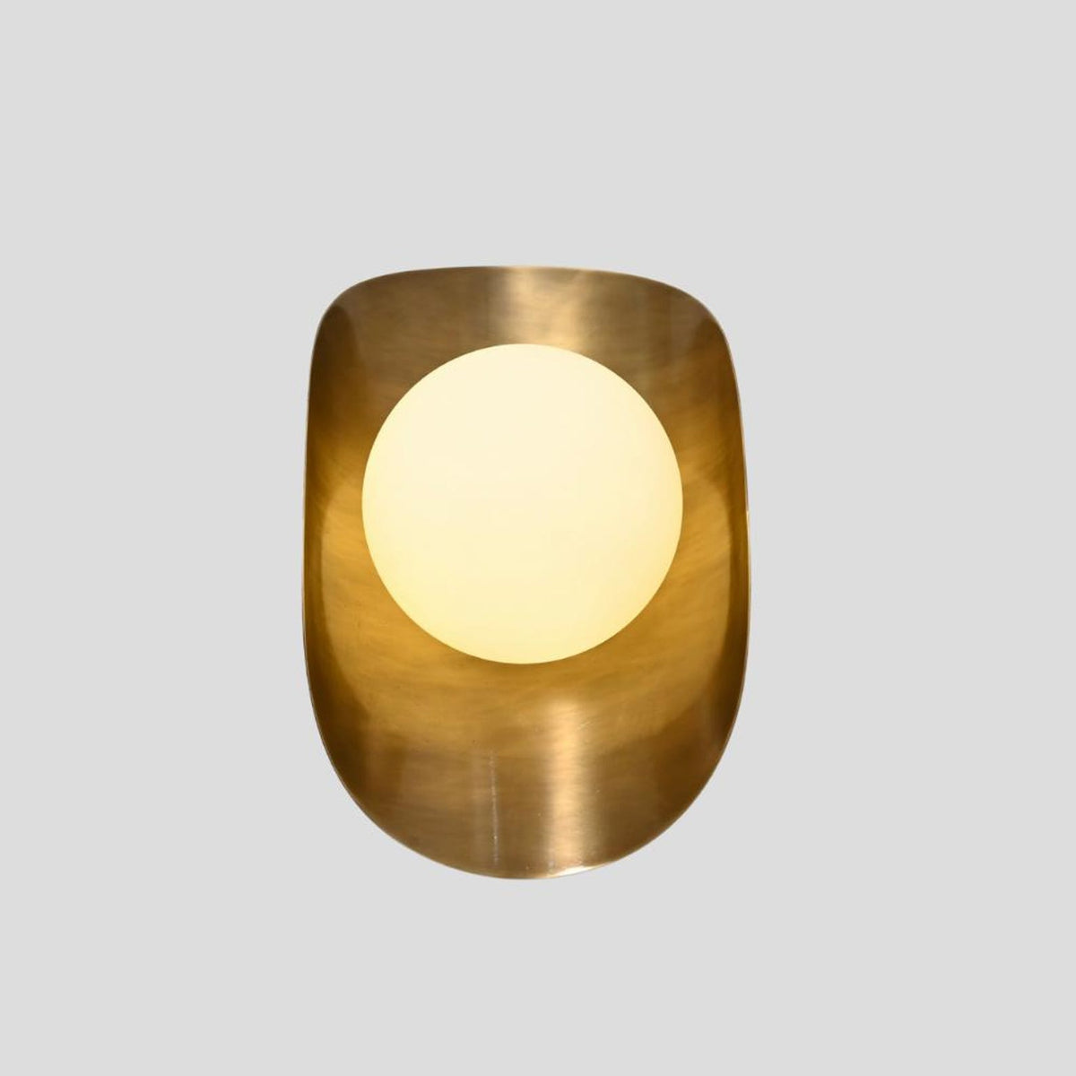 Brass wall sconce with frosted glass globe glowing warmly, emphasizing lacquer-coated brushed brass housing.