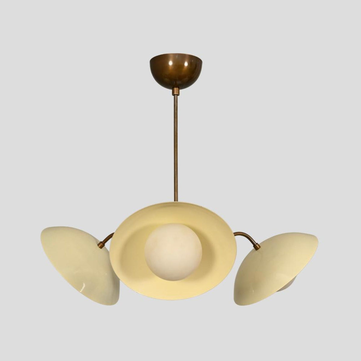 Artistic underside view of a 3-light brass chandelier featuring cream bowl shades and central brass sphere body.