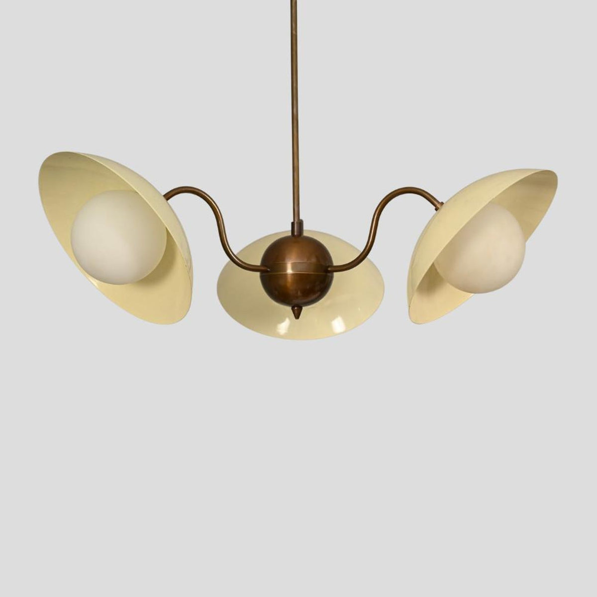 Customizable brass chandelier with three cream enamel shades, designed for living rooms, dining areas, or boutique interiors.
