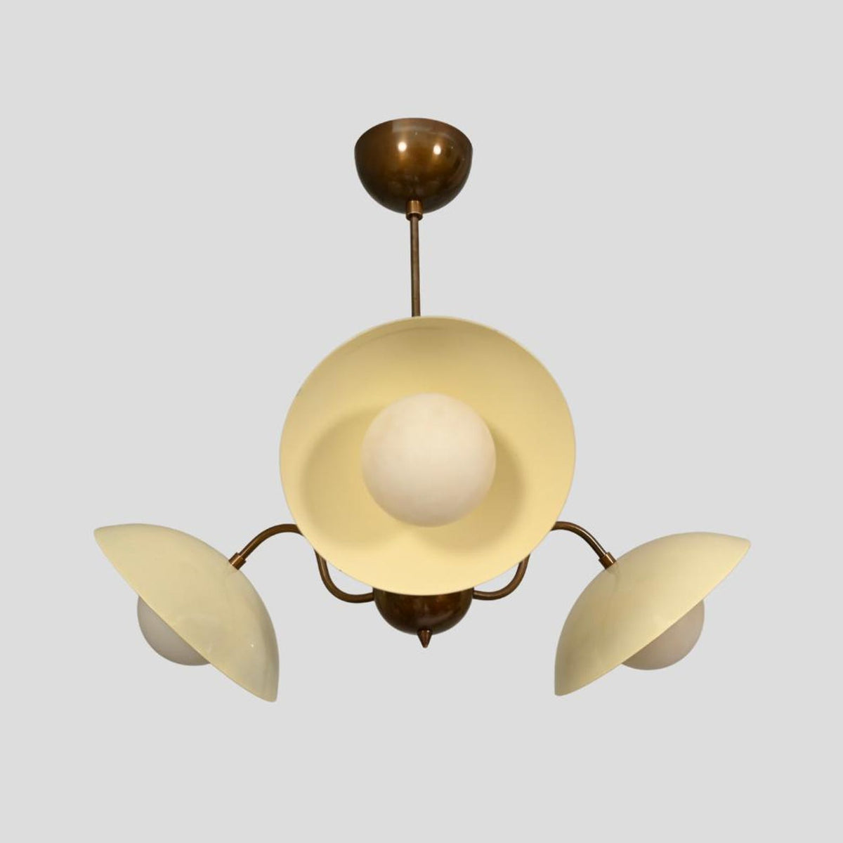 Mid-century style chandelier with brass frame, three cream lacquer-coated shades, and globe bulbs.