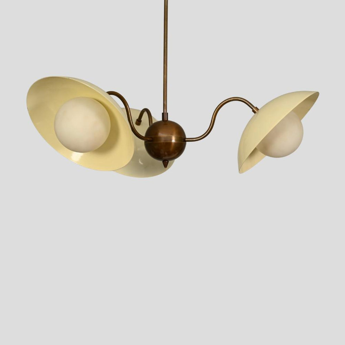 Elegant brass chandelier with curved arms, cream enamel shades, and frosted glass globes for ambient lighting.