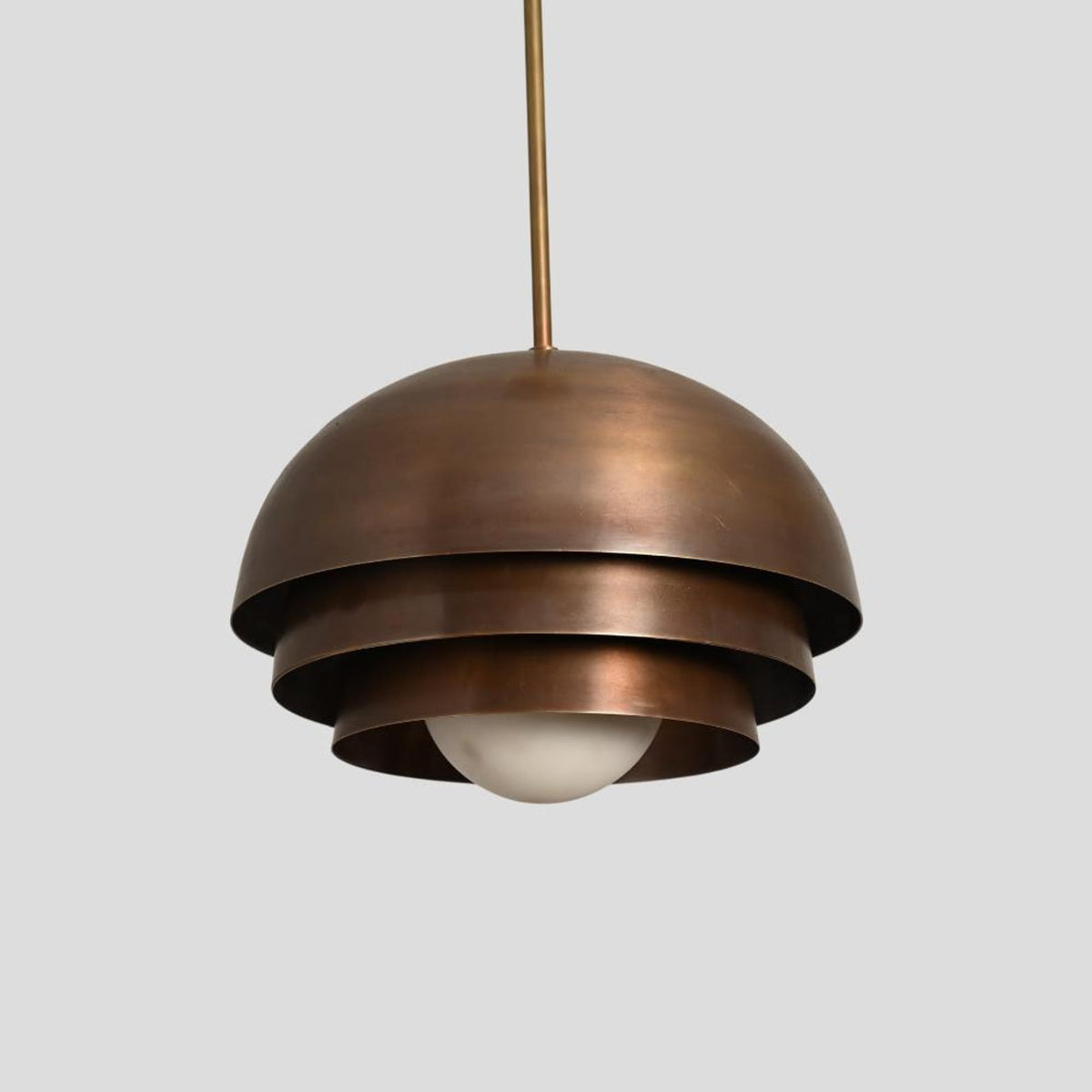 Industrial brass dome pendant with tiered structure and antique patina finish, crafted for elegant interior spaces.