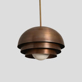 Industrial brass dome pendant with tiered structure and antique patina finish, crafted for elegant interior spaces.