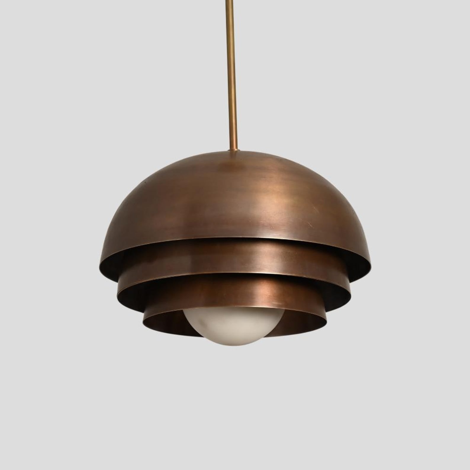 Industrial brass dome pendant with tiered structure and antique patina finish, crafted for elegant interior spaces.