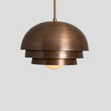 Layered dome brass pendant lamp with industrial patina finish, designed for stylish modern interiors.
