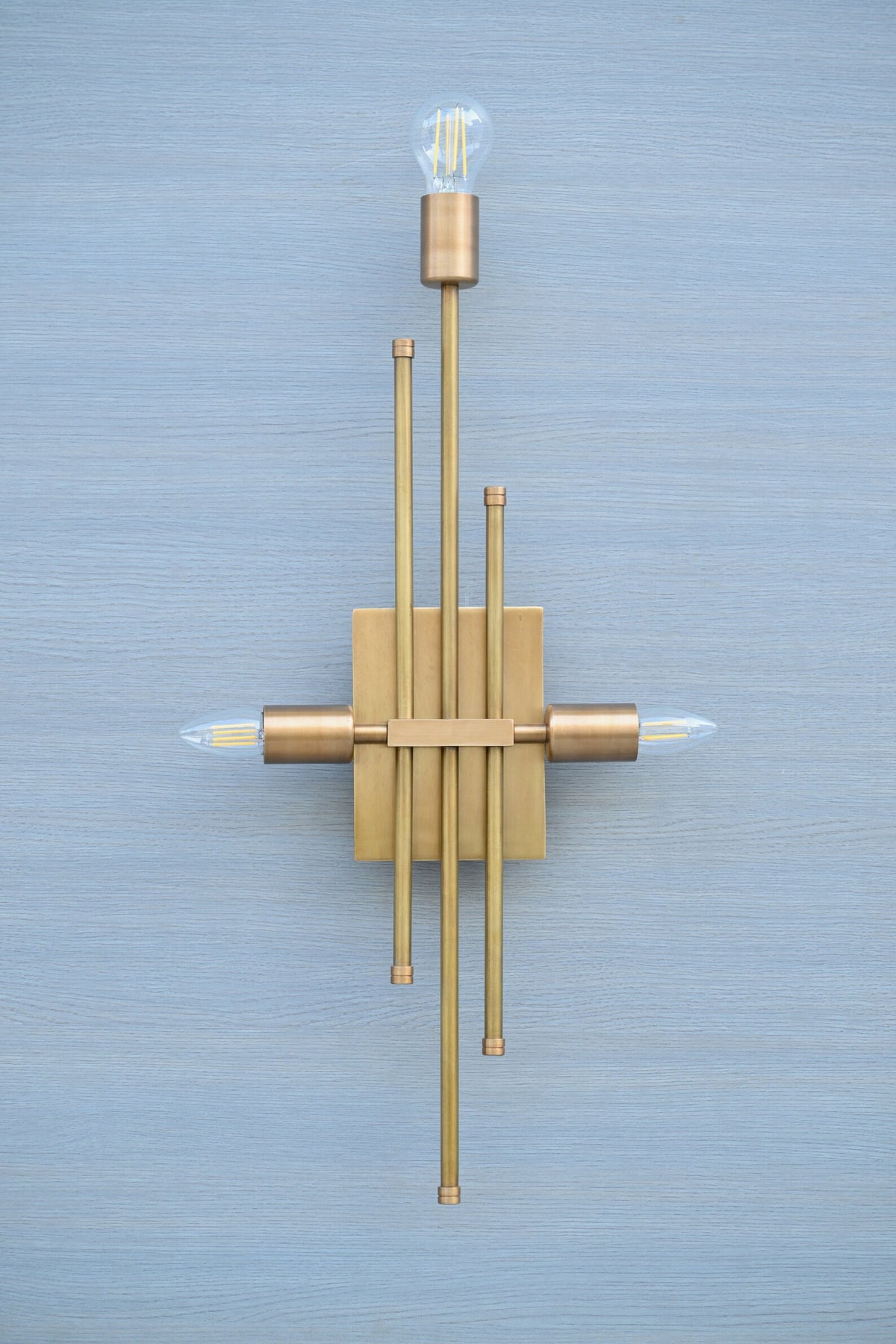 Front view of brass linear wall sconce with geometric rod arrangement and three light holders, handmade luxury wall lighting.