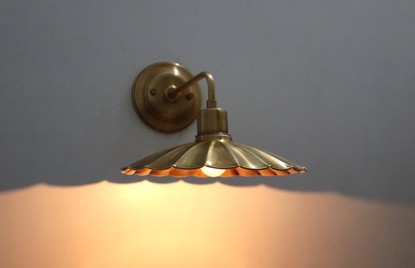Lit brass wall sconce with scalloped disc shade casting a warm ambient glow on the wall below.